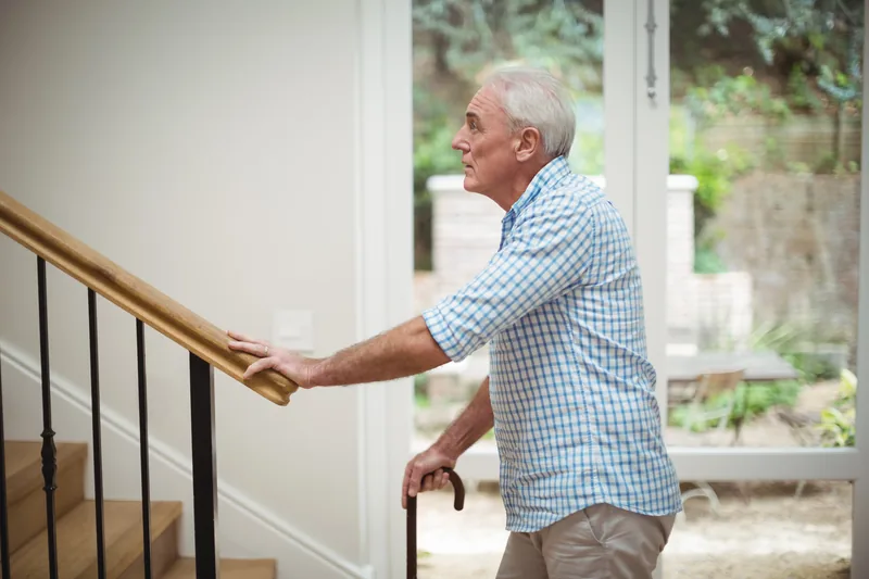 Homme senior montant un escalier droit en tenant la main courante